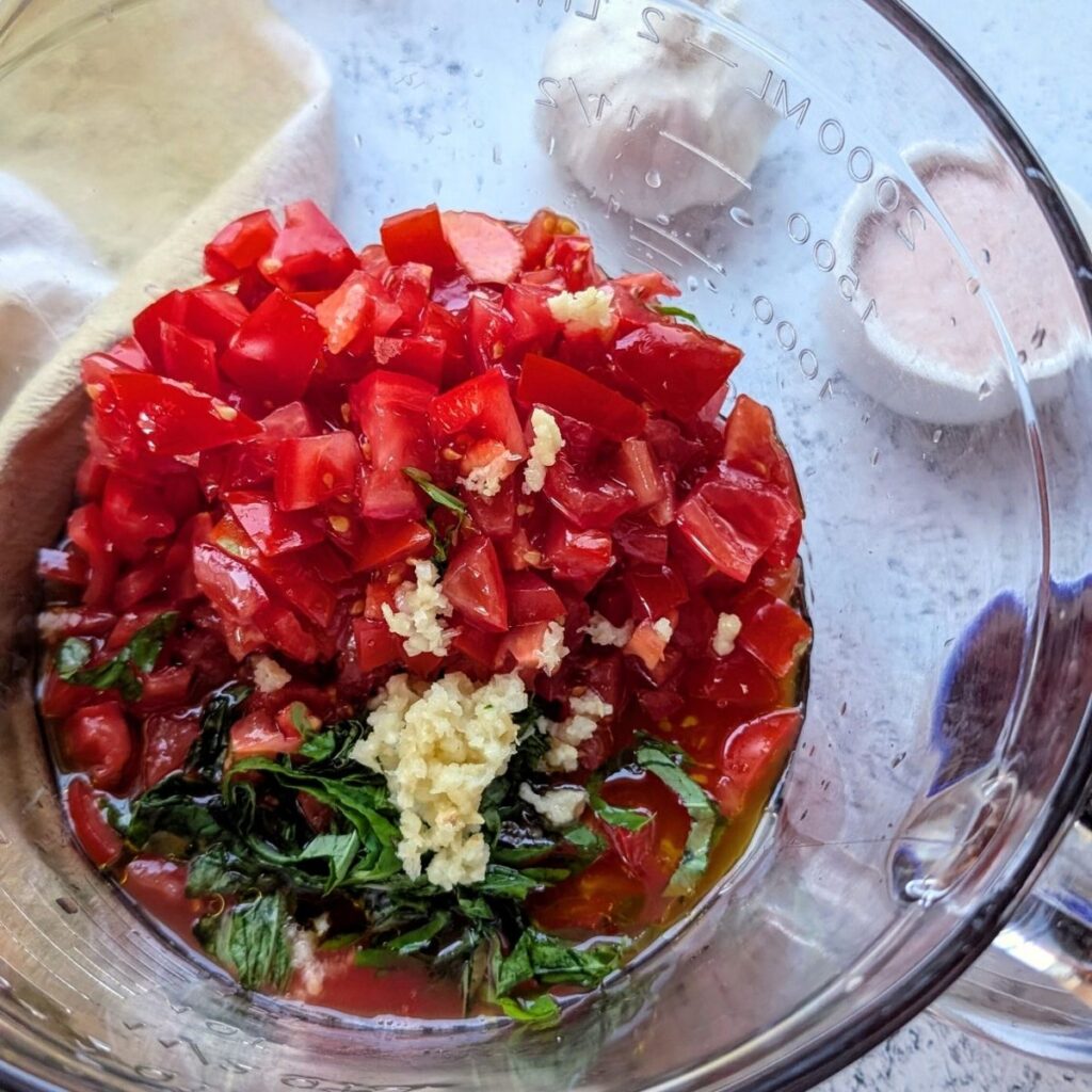 a bowl with fresh tomatoes, garlic, and basil leaves chopped into thin slices.