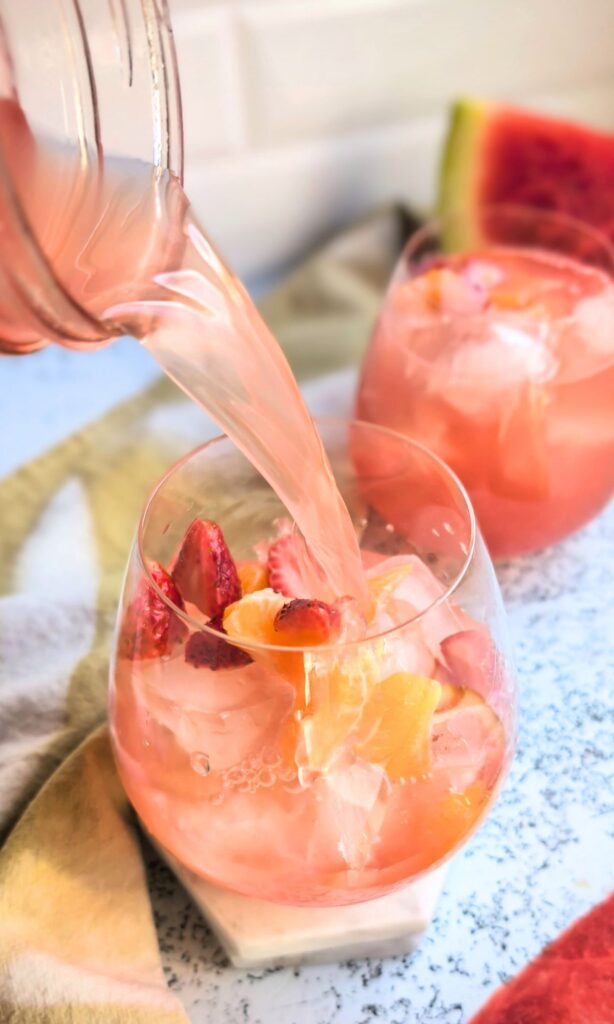 sangria being poured into a wine glass over ice for a tasty summer cocktail