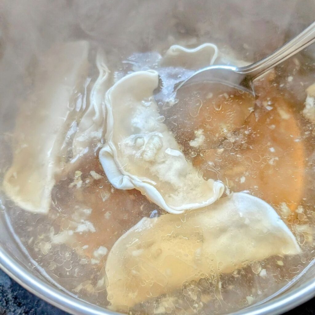 frozen dumpling soup in a pot with soy sauce and bok choy.