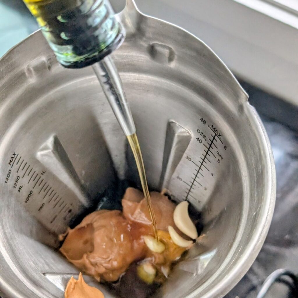 olive oil being added to a blender for peanut sauce with peanut butter.