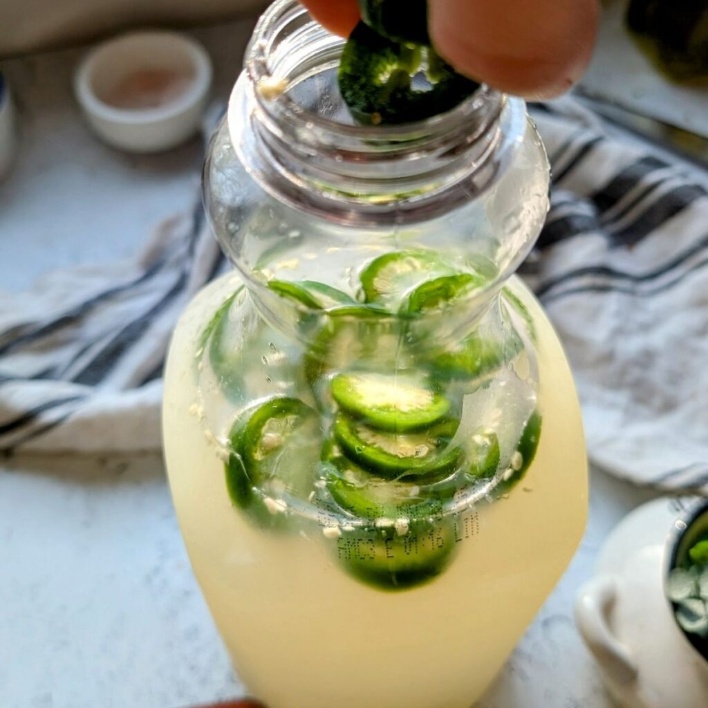 a hand adding sliced peppers into lime lemonade with tequila recipe