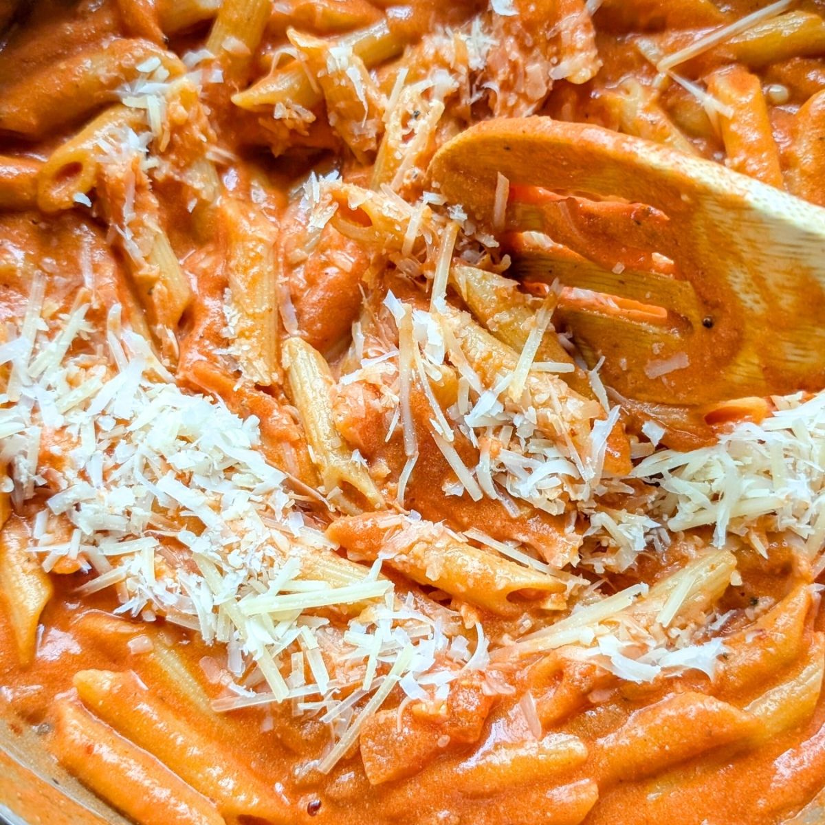 parmesan cheese being stirred into penne alla vodka sauce from camine's