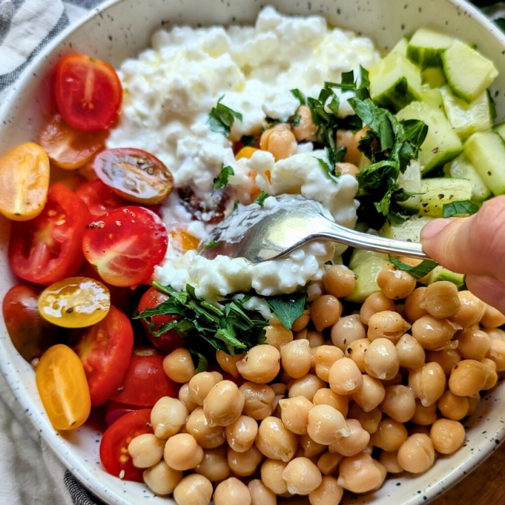 a spoon stirring cottage cheese into cucumber and fresh herbs with garbanzo beans for a vegetarian protein salad.