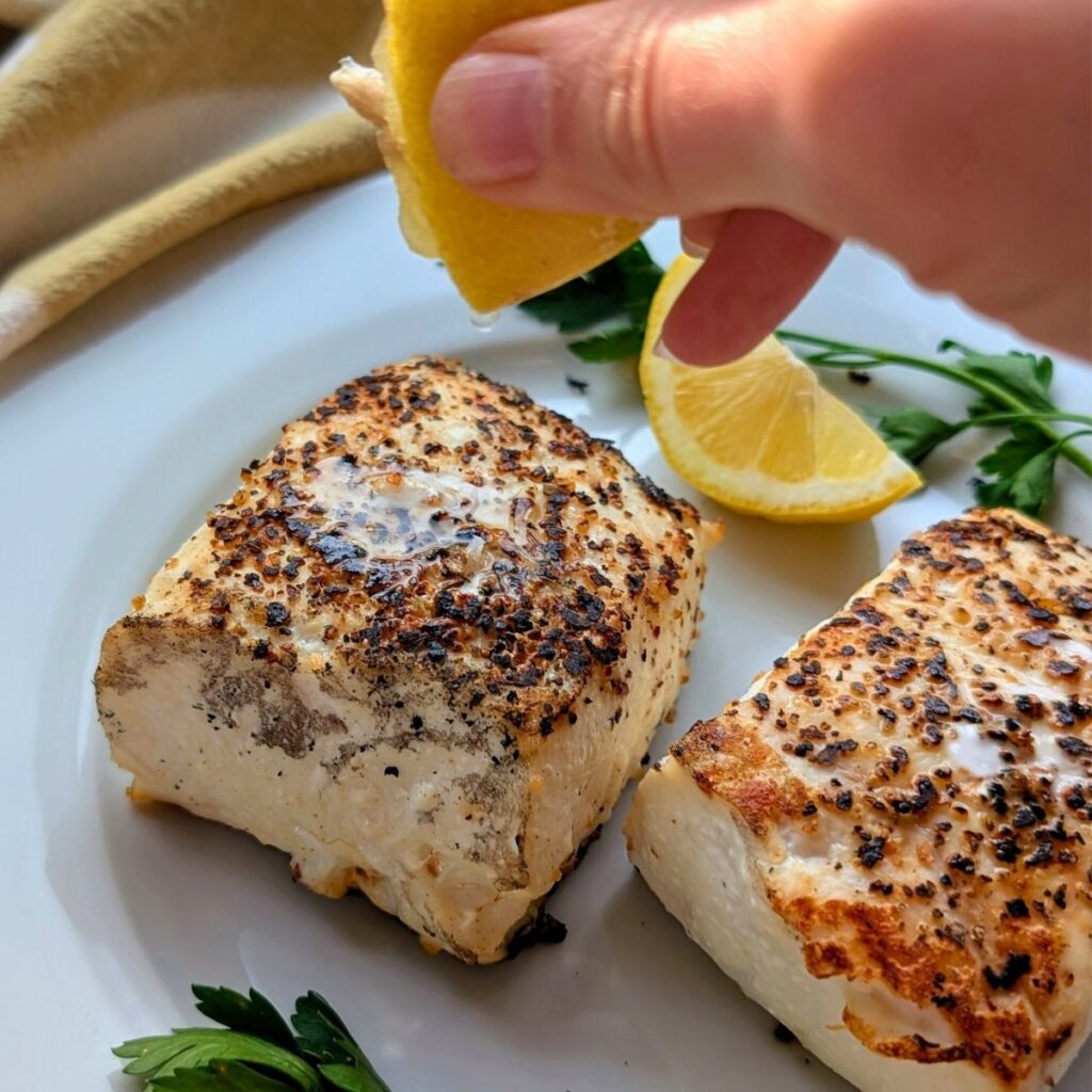 fresh lemon squeezed over grilled halibut on a ceramic grill.