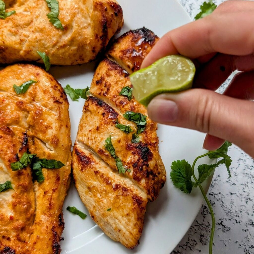 a hand squeezing fresh lime over the air fried mango chicken breasts for a quick and easy dinner idea.